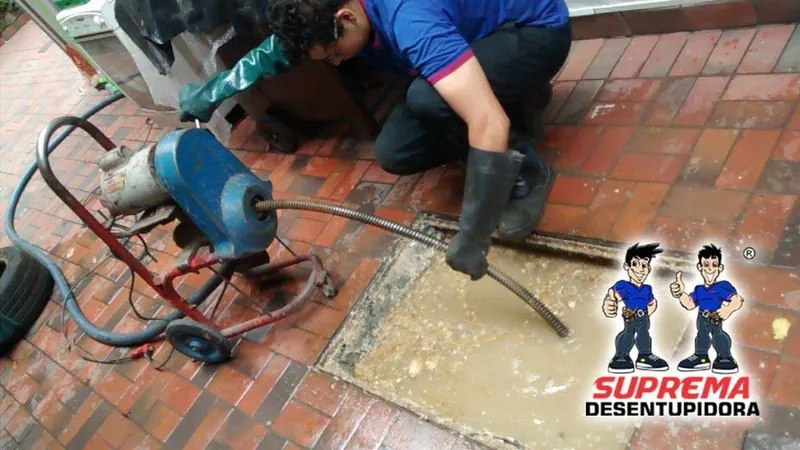 Técnico da Suprema Desentupidora desentupindo caixa de gordura com máquina rotativa; atendimento em Castelo, Belo Horizonte